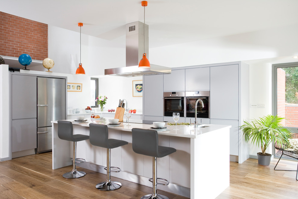 Mittelgroße Moderne Küche in L-Form mit flächenbündigen Schrankfronten, Küchengeräten aus Edelstahl, hellem Holzboden, Kücheninsel, weißer Arbeitsplatte, grauen Schränken und Unterbauwaschbecken in Sonstige