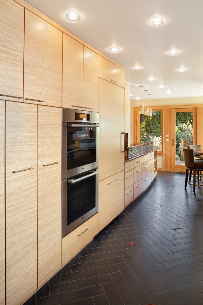 Свежая идея для дизайна: кухня в современном стиле с техникой под мебельный фасад, плоскими фасадами, светлыми деревянными фасадами и черным полом - отличное фото интерьера