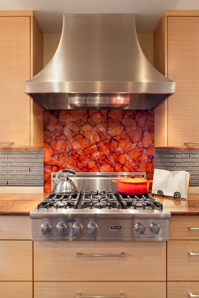 Moderne Küche mit Küchengeräten aus Edelstahl, flächenbündigen Schrankfronten, hellbraunen Holzschränken, Granit-Arbeitsplatte, Küchenrückwand in Rot und Glasrückwand in Portland