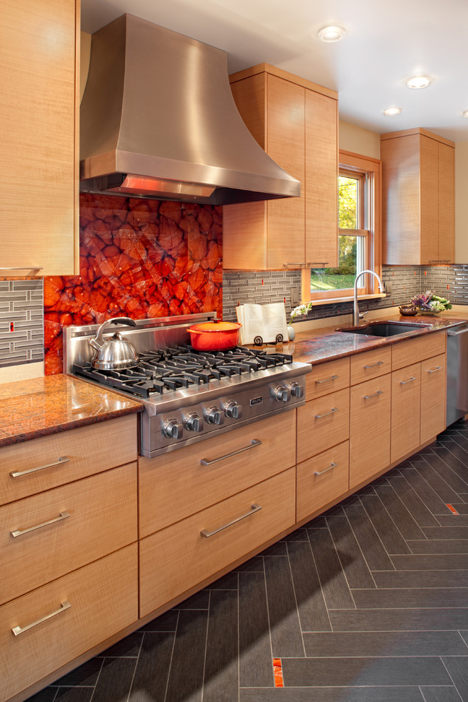Foto di una cucina design con elettrodomestici in acciaio inossidabile, lavello sottopiano, ante lisce, ante in legno scuro, top in granito, paraspruzzi rosso, paraspruzzi con lastra di vetro e pavimento grigio