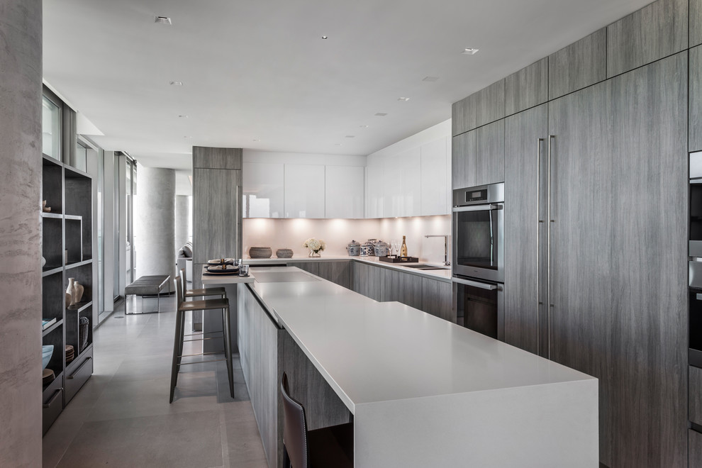 Contemporary l-shaped kitchen in Miami with a double-bowl sink, flat-panel cabinets, white cabinets, white splashback, stainless steel appliances, an island, grey floors and white worktops.
