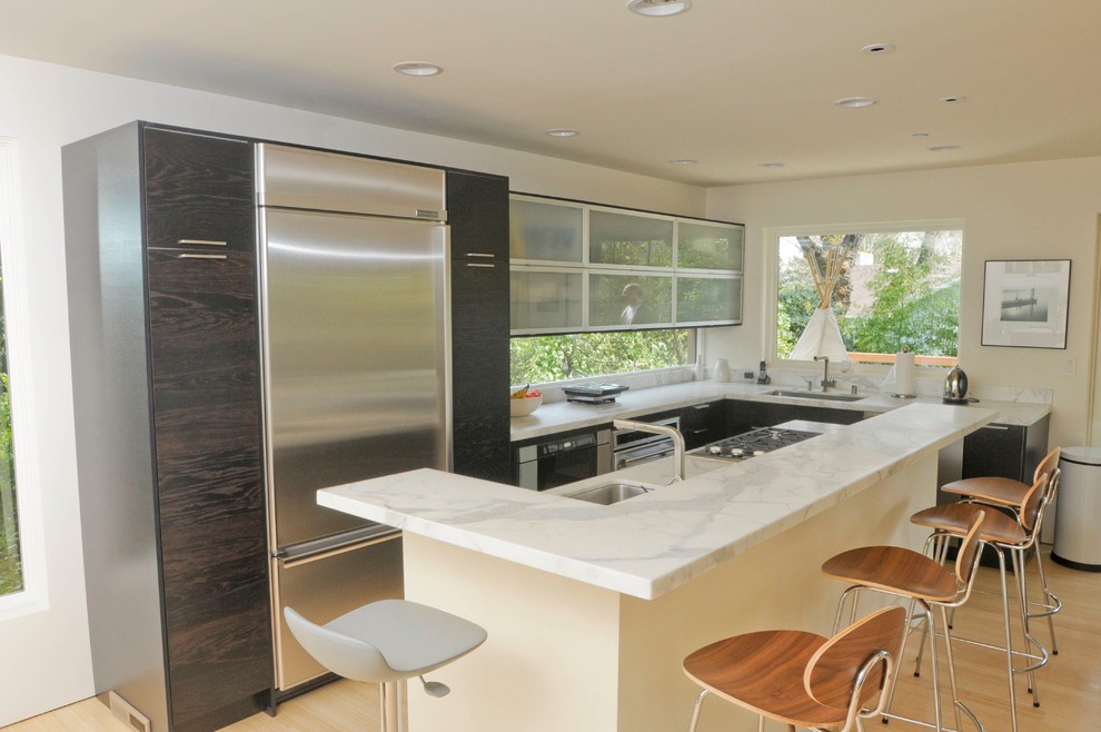 Cette photo montre une cuisine tendance en bois foncé avec plan de travail en marbre, un placard à porte plane et un électroménager en acier inoxydable.