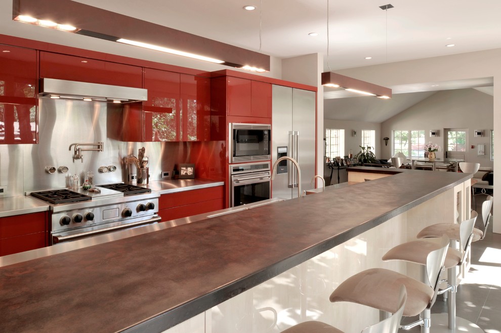 Bild på ett funkis kök med öppen planlösning, med släta luckor, bänkskiva i rostfritt stål, röda skåp, stänkskydd med metallisk yta, stänkskydd i metallkakel och rostfria vitvaror
