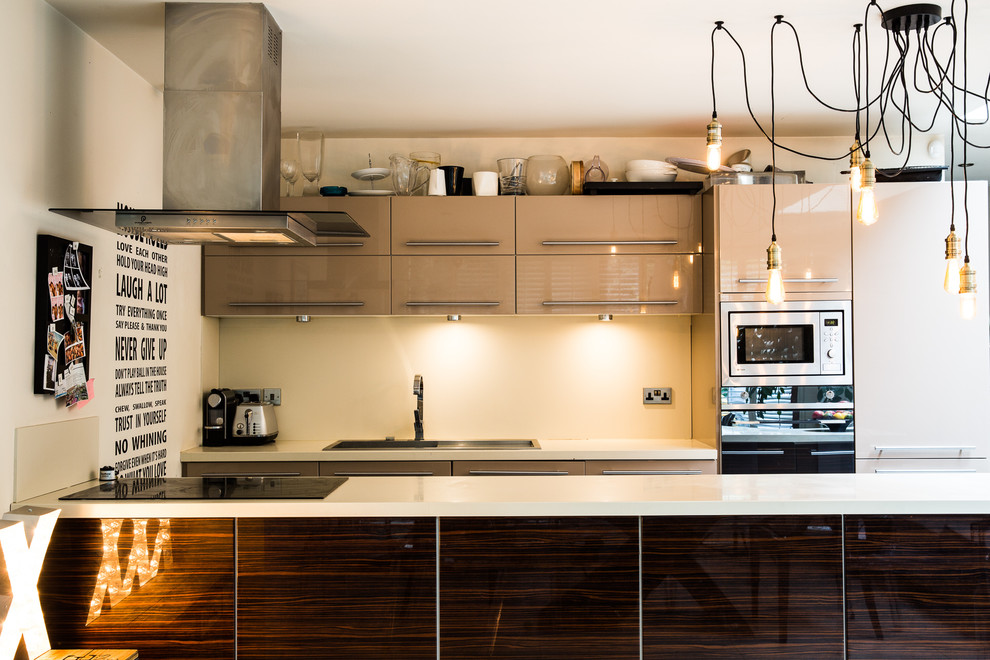 Moderne Küche mit Einbauwaschbecken, flächenbündigen Schrankfronten, beigen Schränken, Küchenrückwand in Beige und Elektrogeräten mit Frontblende in London