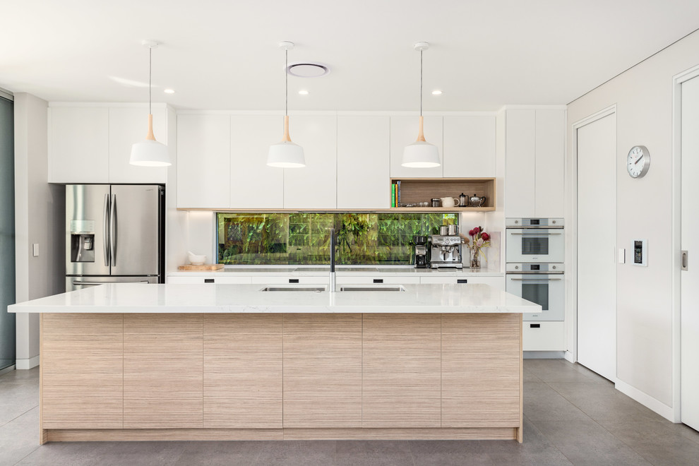 Immagine di una cucina minimal con lavello sottopiano, ante lisce, ante bianche, paraspruzzi a finestra, elettrodomestici in acciaio inossidabile, pavimento grigio e top bianco
