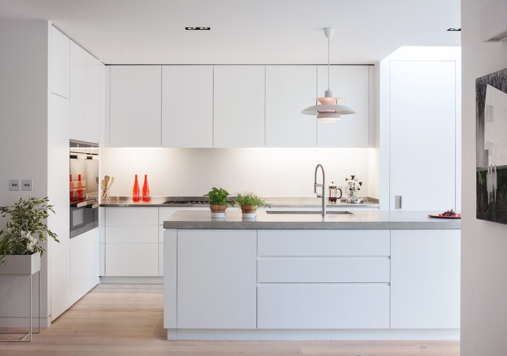 Exempel på ett stort modernt kök, med en undermonterad diskho, släta luckor, vita skåp, vitt stänkskydd, rostfria vitvaror, ljust trägolv, en köksö och beiget golv