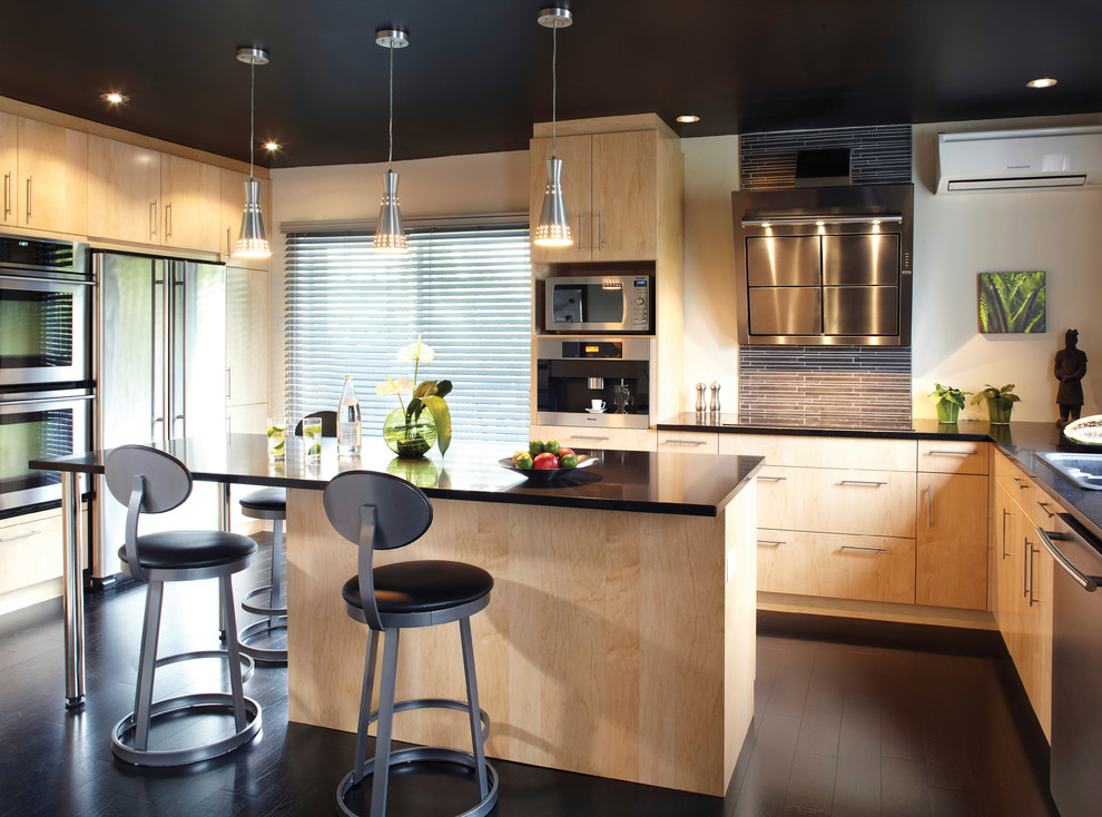 Moderne Küche in U-Form mit Einbauwaschbecken, flächenbündigen Schrankfronten, hellen Holzschränken, Küchenrückwand in Schwarz und Küchengeräten aus Edelstahl