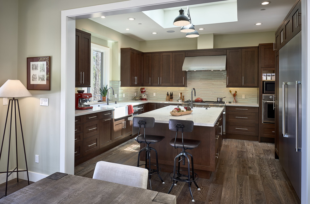 Example of a mid-sized trendy l-shaped medium tone wood floor and brown floor eat-in kitchen design in San Francisco with a farmhouse sink, flat-panel cabinets, medium tone wood cabinets, granite countertops, green backsplash, glass tile backsplash, stainless steel appliances, an island and white countertops