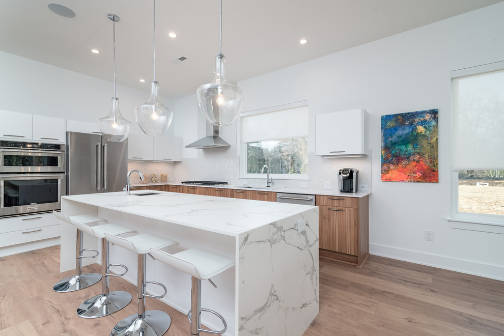 Inspiration for a mid-sized contemporary l-shaped laminate floor and brown floor eat-in kitchen remodel in Charlotte with an undermount sink, flat-panel cabinets, white cabinets, quartz countertops, white backsplash, porcelain backsplash, stainless steel appliances and an island