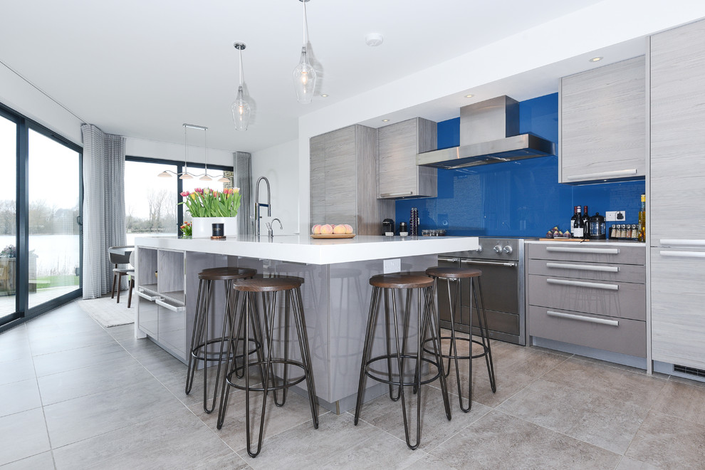 Moderne Küche mit flächenbündigen Schrankfronten, grauen Schränken, Küchenrückwand in Blau, Glasrückwand, Elektrogeräten mit Frontblende, Kücheninsel, grauem Boden und weißer Arbeitsplatte in Berkshire