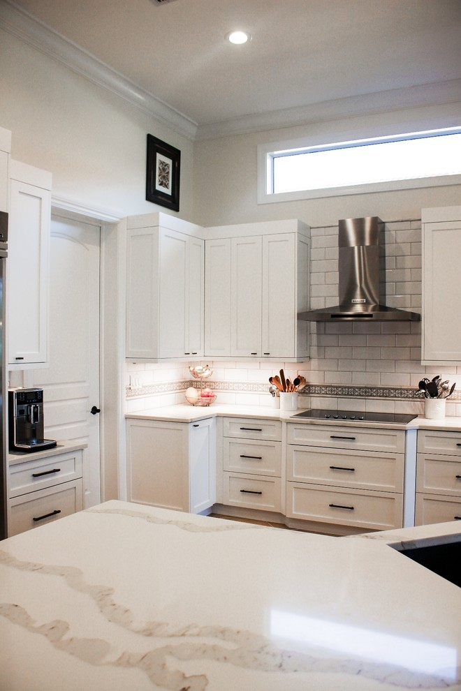 Foto på ett stort funkis vit kök, med en dubbel diskho, skåp i shakerstil, vita skåp, granitbänkskiva, vitt stänkskydd, stänkskydd i tunnelbanekakel, rostfria vitvaror, klinkergolv i porslin, en köksö och beiget golv