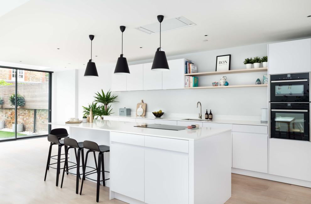 Zweizeilige Moderne Küche mit Unterbauwaschbecken, flächenbündigen Schrankfronten, schwarzen Elektrogeräten, hellem Holzboden, Kücheninsel, beigem Boden und weißer Arbeitsplatte in London