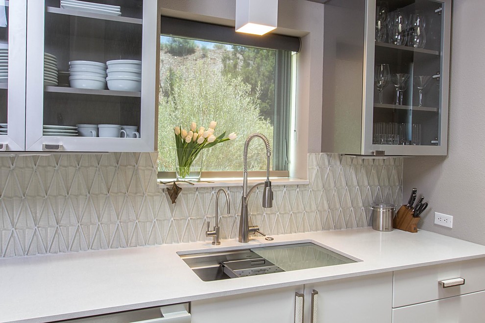 Inspiration for a small contemporary kitchen/diner in Albuquerque with a submerged sink, glass-front cabinets, white cabinets, engineered stone countertops, white splashback, glass sheet splashback and stainless steel appliances.