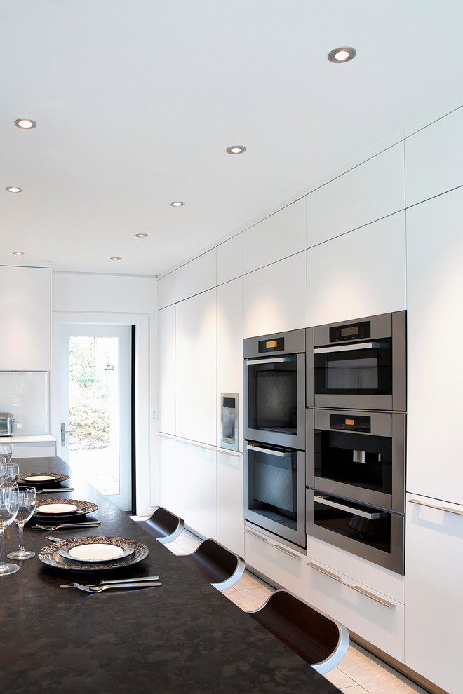 Modern inredning av ett stort kök, med en enkel diskho, släta luckor, vita skåp, marmorbänkskiva, vitt stänkskydd, glaspanel som stänkskydd, rostfria vitvaror, klinkergolv i keramik och en köksö