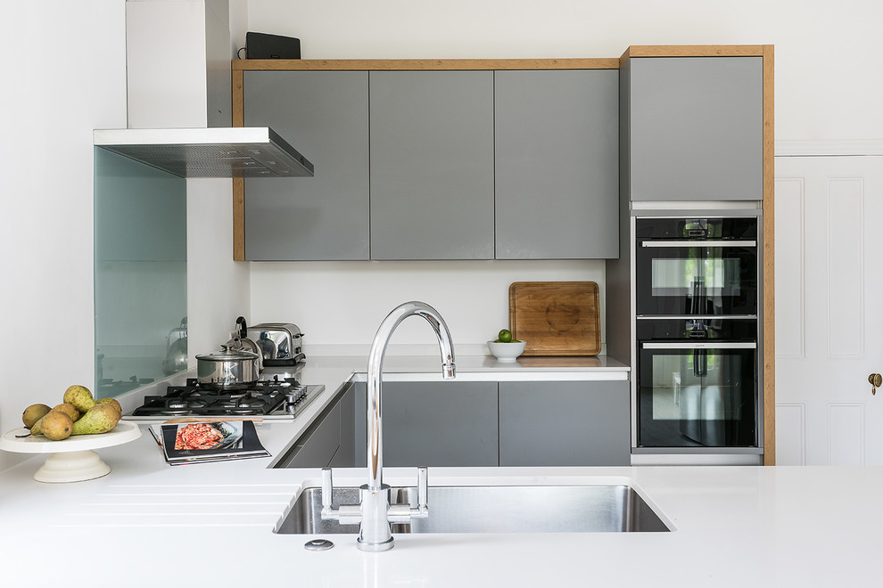 Small trendy kitchen photo in London with an undermount sink, flat-panel cabinets, gray cabinets, glass sheet backsplash, black appliances and a peninsula