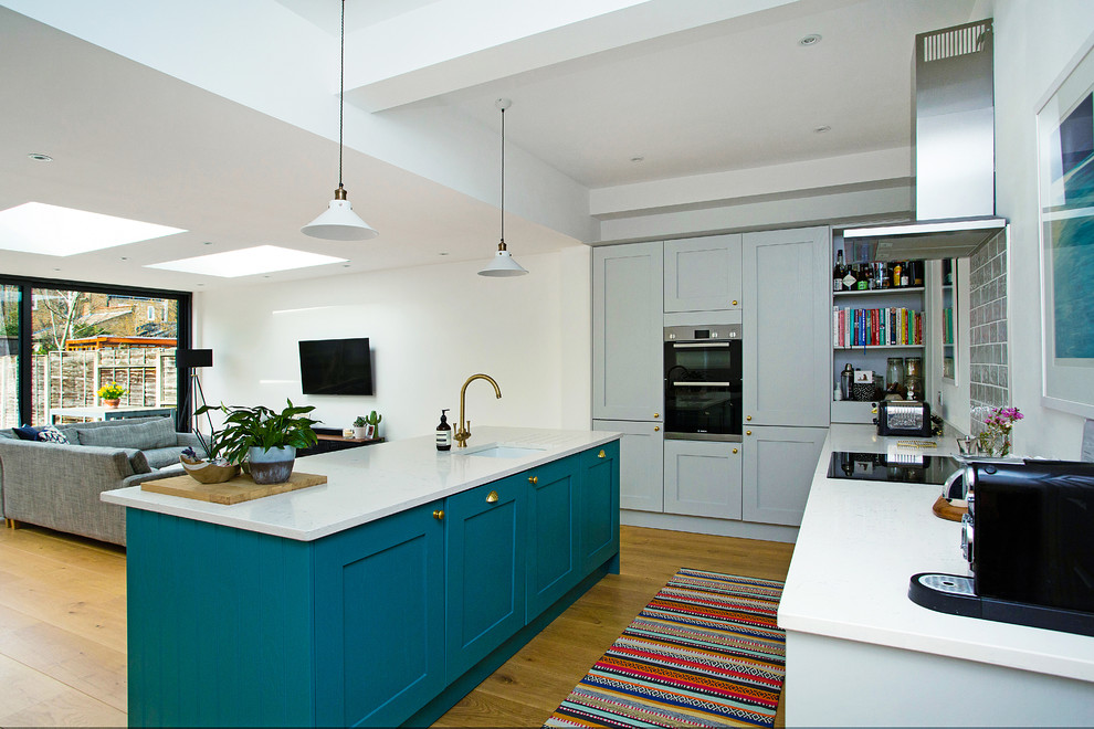 Modern inredning av ett stort vit vitt kök, med en undermonterad diskho, skåp i shakerstil, grå skåp, bänkskiva i kvartsit, grönt stänkskydd, stänkskydd i keramik, en köksö, svarta vitvaror, mellanmörkt trägolv och brunt golv