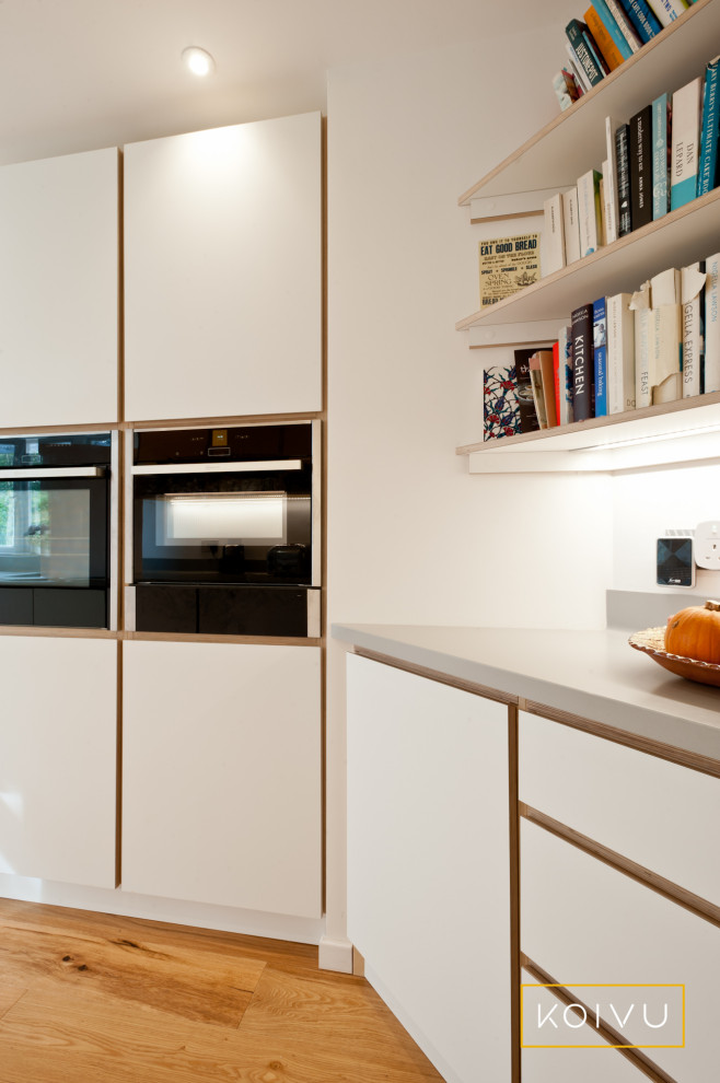 Inspiration for a medium sized contemporary galley enclosed kitchen in Kent with a double-bowl sink, flat-panel cabinets, white cabinets, composite countertops, glass sheet splashback, stainless steel appliances, light hardwood flooring, no island and grey worktops.