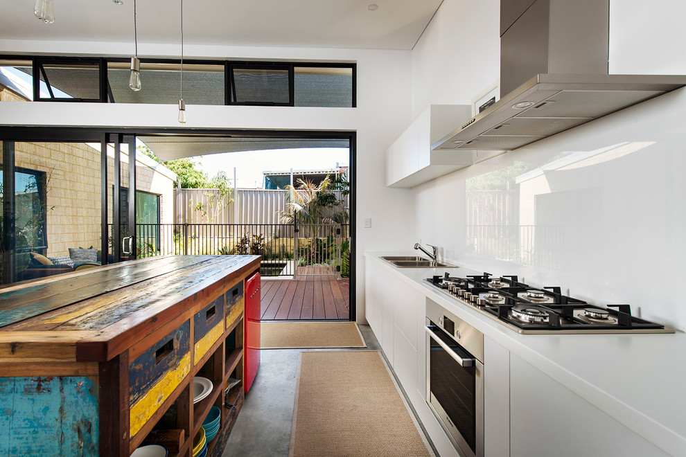 Foto på ett litet funkis linjärt kök, med en dubbel diskho, släta luckor, vita skåp, vitt stänkskydd, betonggolv och en köksö