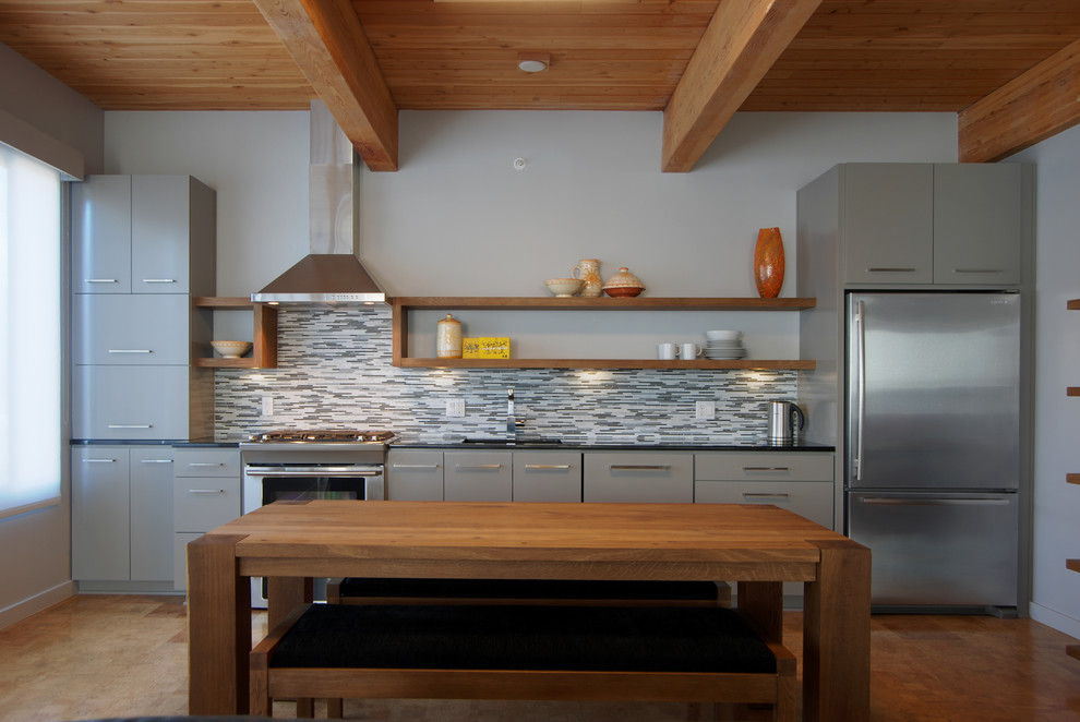 Modelo de cocina comedor lineal contemporánea con electrodomésticos de acero inoxidable, armarios con paneles lisos, puertas de armario grises, salpicadero verde y salpicadero de azulejos en listel