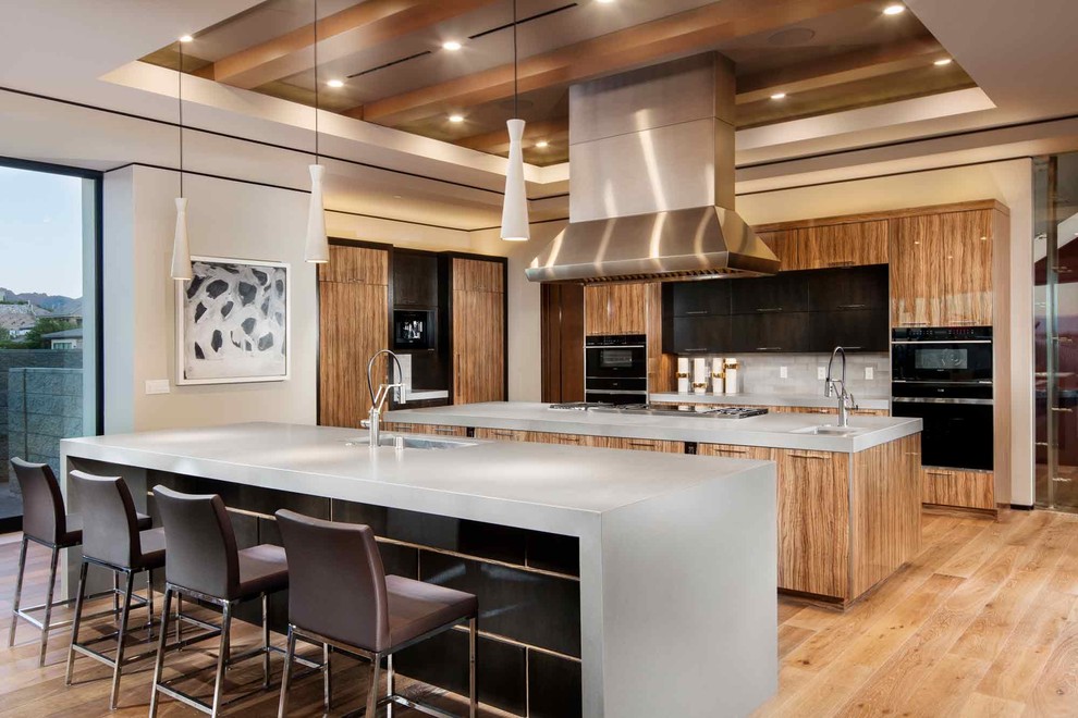 Design ideas for an expansive contemporary kitchen in Phoenix with a submerged sink, flat-panel cabinets, grey splashback, black appliances, light hardwood flooring and multiple islands.