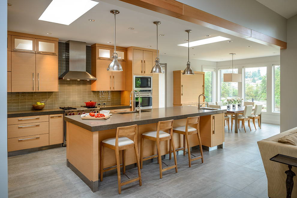 Inredning av ett modernt kök med öppen planlösning, med en rustik diskho, släta luckor, skåp i ljust trä, brunt stänkskydd, stänkskydd i tunnelbanekakel och rostfria vitvaror