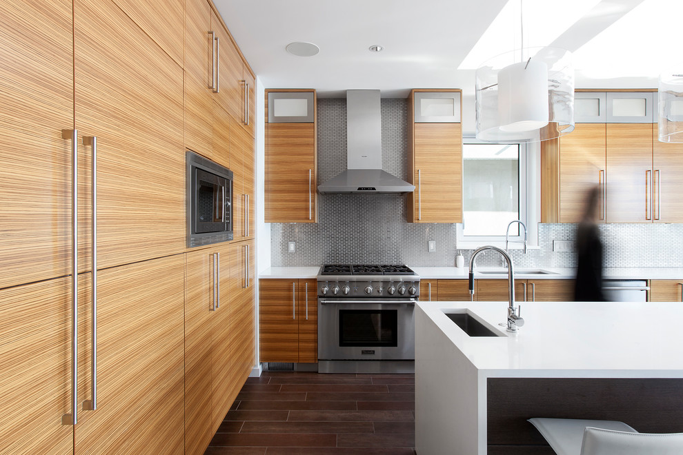 Moderne Wohnküche in L-Form mit Unterbauwaschbecken, Küchenrückwand in Metallic, Rückwand aus Metallfliesen, Küchengeräten aus Edelstahl, Keramikboden, braunem Boden, flächenbündigen Schrankfronten, hellbraunen Holzschränken, Kücheninsel und weißer Arbeitsplatte in Vancouver