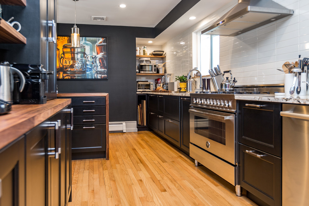 ニューヨークにある中くらいなコンテンポラリースタイルのおしゃれなキッチン (アンダーカウンターシンク、落し込みパネル扉のキャビネット、黒いキャビネット、木材カウンター、白いキッチンパネル、シルバーの調理設備、茶色いキッチンカウンター、サブウェイタイルのキッチンパネル、淡色無垢フローリング、ベージュの床) の写真
