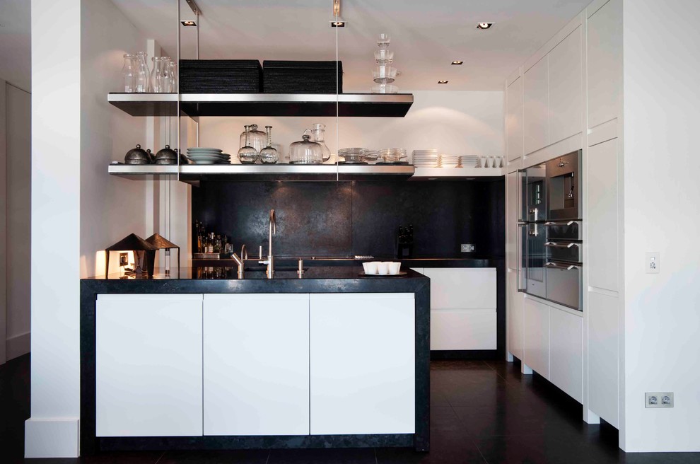 Ejemplo de cocina contemporánea con armarios con paneles lisos, salpicadero negro, electrodomésticos de acero inoxidable y con blanco y negro