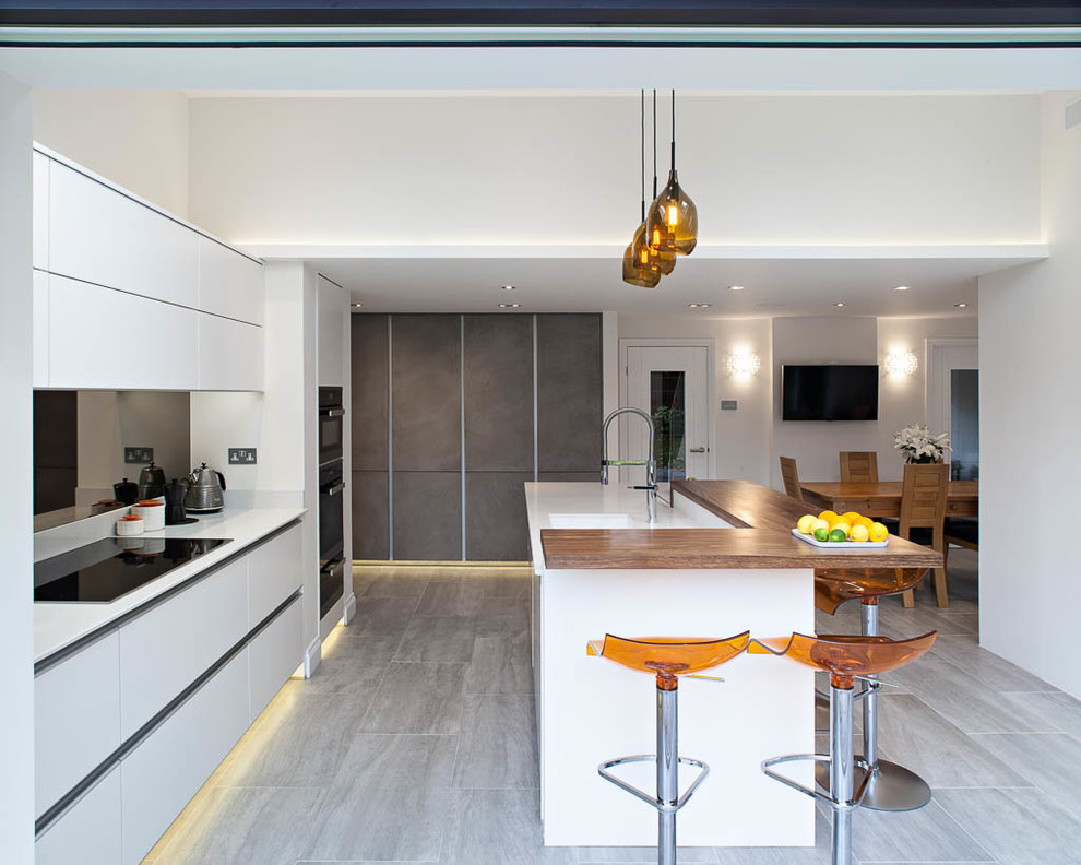 Einzeilige, Mittelgroße Moderne Wohnküche mit Unterbauwaschbecken, flächenbündigen Schrankfronten, weißen Schränken, Elektrogeräten mit Frontblende, Halbinsel und grauem Boden in Hertfordshire