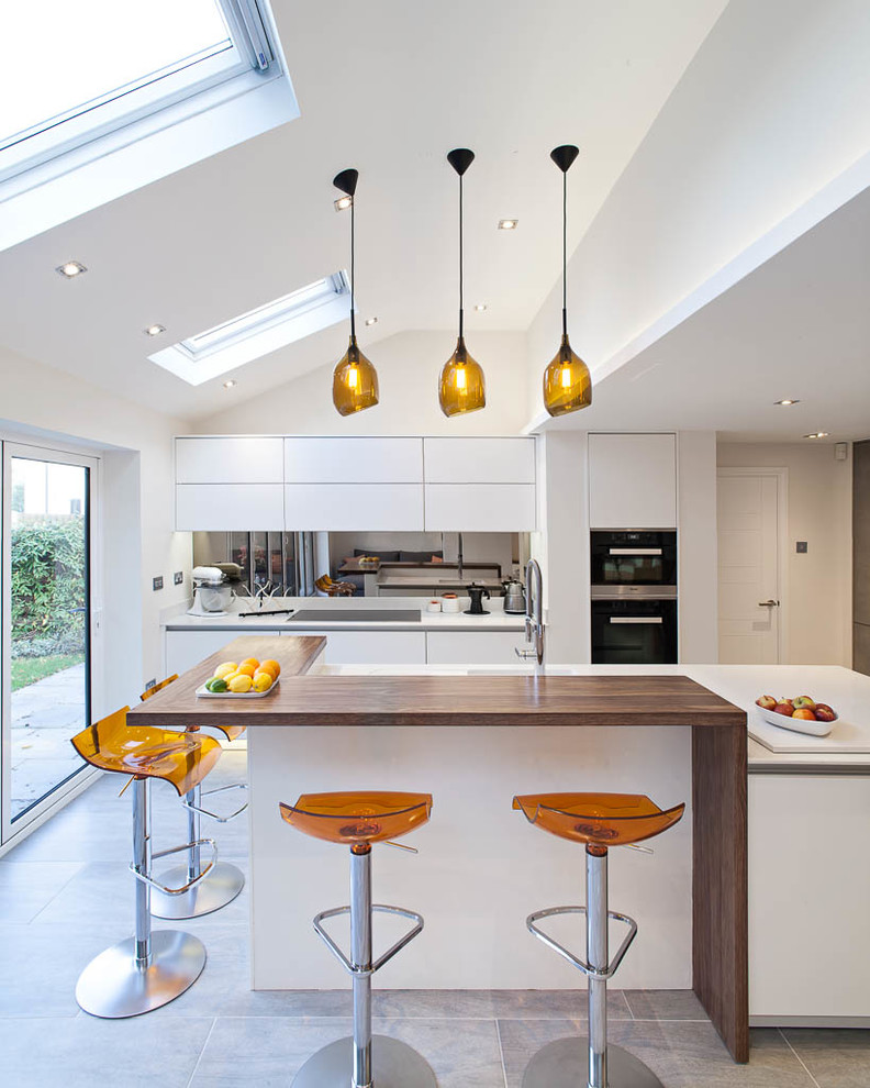 Moderne Küche mit flächenbündigen Schrankfronten, weißen Schränken, Rückwand aus Spiegelfliesen, schwarzen Elektrogeräten, Kücheninsel und grauem Boden in Hertfordshire