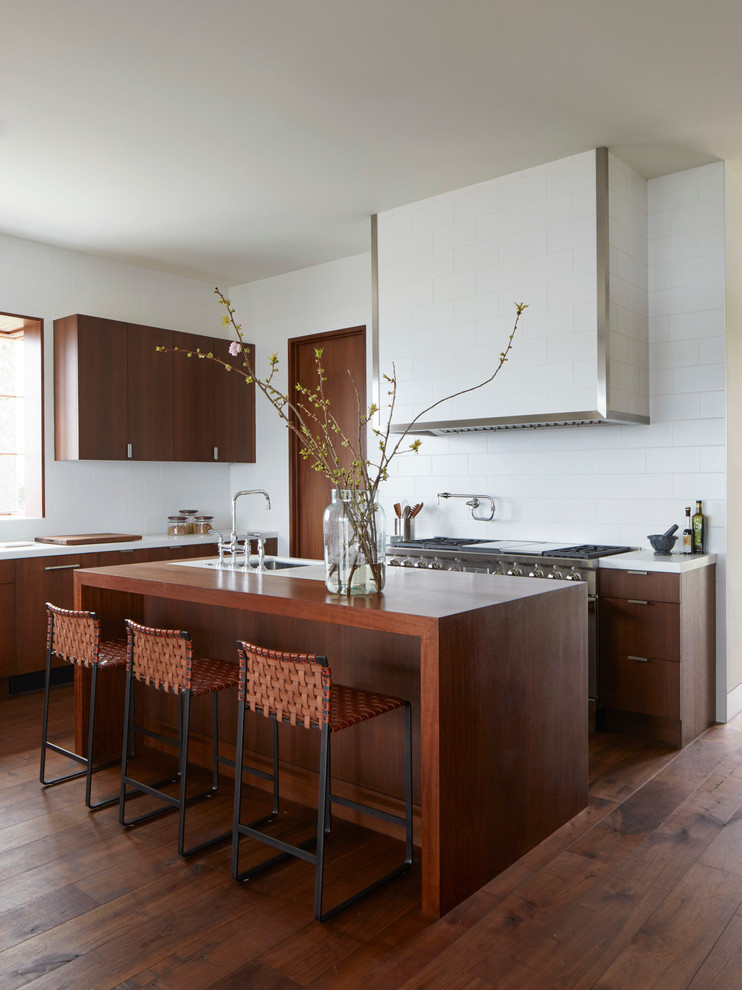 Inredning av ett modernt kök, med marmorbänkskiva, mellanmörkt trägolv, en köksö, släta luckor, skåp i mellenmörkt trä, vitt stänkskydd och rostfria vitvaror