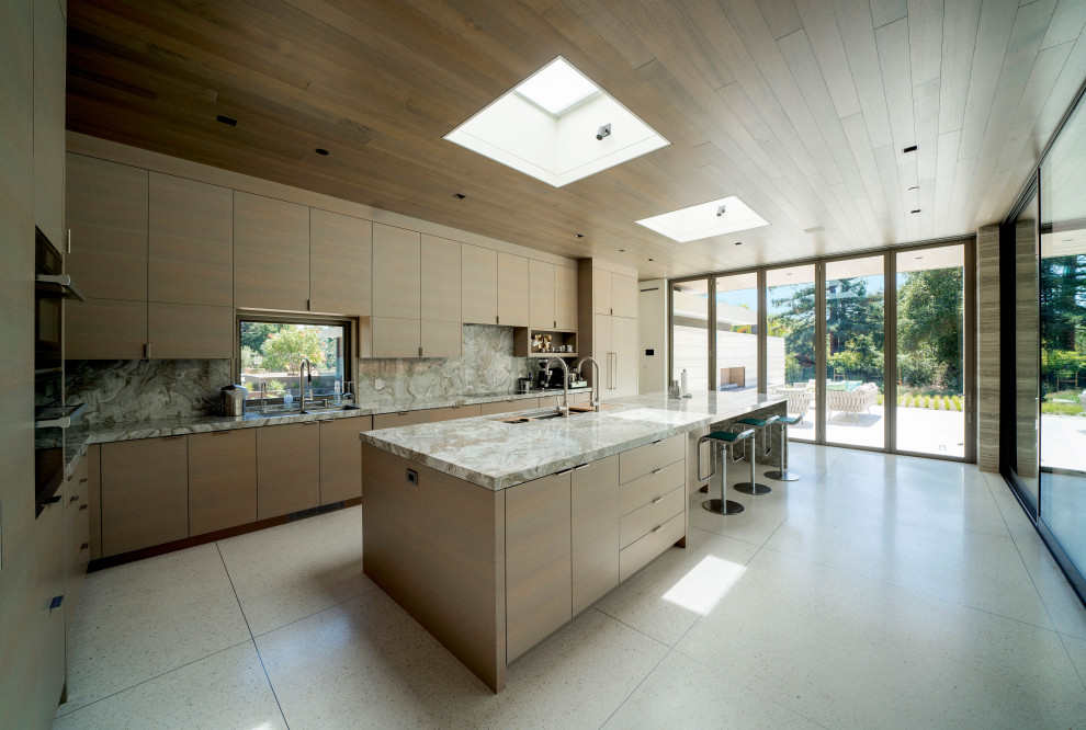 Inspiration for a large contemporary l-shaped kitchen in San Francisco with a submerged sink, flat-panel cabinets, granite worktops, stone slab splashback, stainless steel appliances, terrazzo flooring, an island, beige floors, light wood cabinets, beige splashback and beige worktops.
