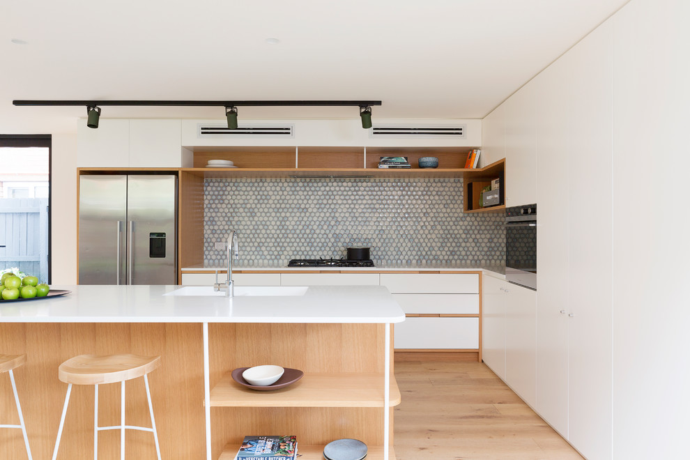 Foto på ett funkis vit kök, med en integrerad diskho, släta luckor, vita skåp, blått stänkskydd, stänkskydd i mosaik, rostfria vitvaror, ljust trägolv, en köksö och beiget golv