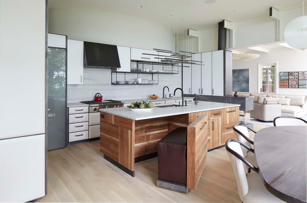 Contemporary open plan kitchen in Chicago with a submerged sink, flat-panel cabinets, white cabinets, white splashback, marble splashback, stainless steel appliances, light hardwood flooring, an island and beige floors.