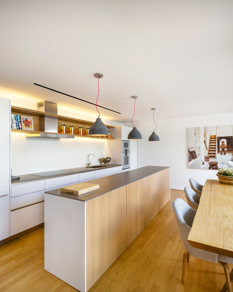 Idéer för att renovera ett mellanstort skandinaviskt kök, med en integrerad diskho, släta luckor, vita skåp, vitt stänkskydd, rostfria vitvaror, mellanmörkt trägolv och en köksö