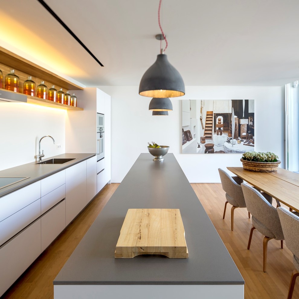 Пример оригинального дизайна: параллельная кухня среднего размера в скандинавском стиле с обеденным столом, монолитной мойкой, плоскими фасадами, белыми фасадами, белым фартуком, техникой из нержавеющей стали, паркетным полом среднего тона и островом