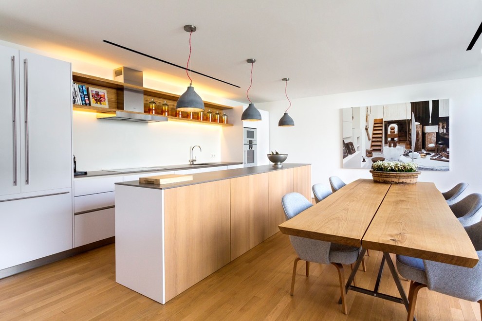 Стильный дизайн: параллельная кухня среднего размера в скандинавском стиле с обеденным столом, плоскими фасадами, белыми фасадами, белым фартуком, техникой из нержавеющей стали, паркетным полом среднего тона, островом и врезной мойкой - последний тренд