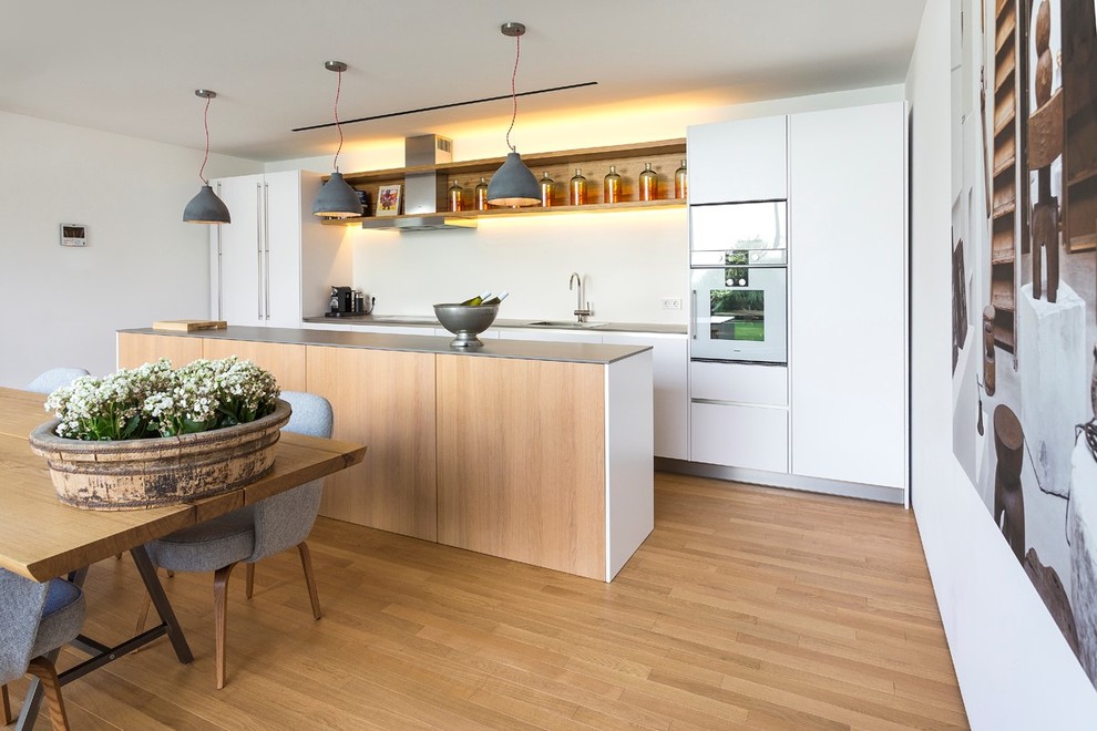 Medium sized scandi galley kitchen/diner in Other with an integrated sink, flat-panel cabinets, white cabinets, white splashback, stainless steel appliances, medium hardwood flooring and an island.