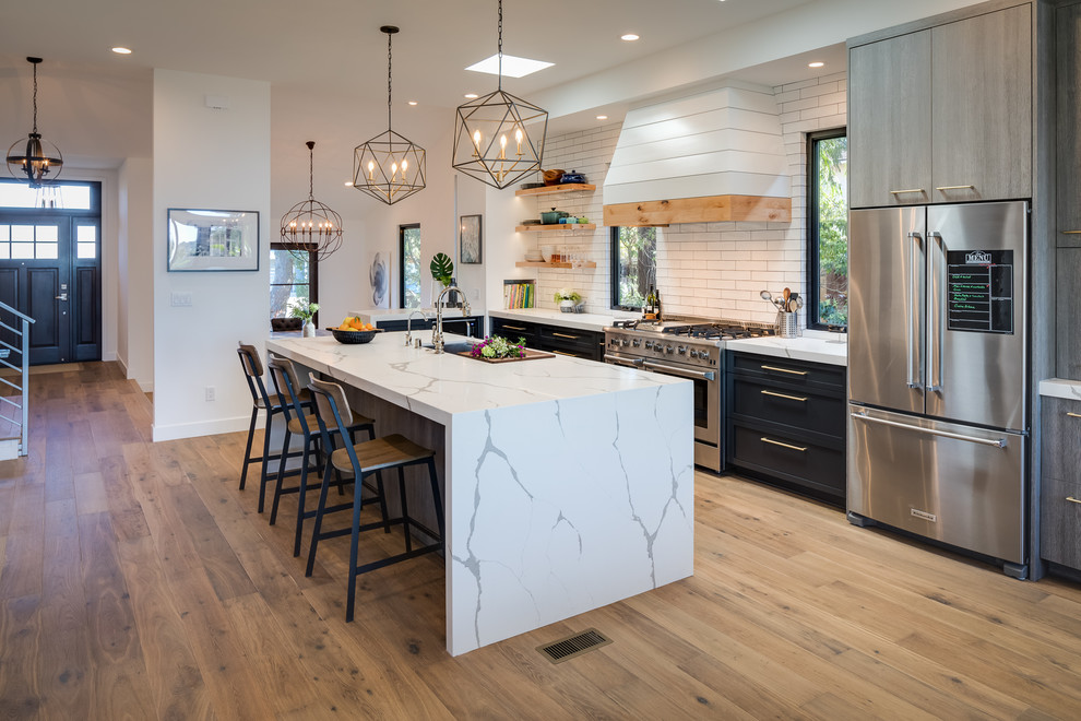 Inspiration for a large contemporary single-wall light wood floor and brown floor open concept kitchen remodel in San Diego with an undermount sink, shaker cabinets, black cabinets, quartz countertops, white backsplash, subway tile backsplash, stainless steel appliances, an island and white countertops
