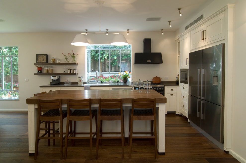 Imagen de cocinas en L actual con electrodomésticos de acero inoxidable, encimera de madera, armarios con paneles empotrados y puertas de armario blancas