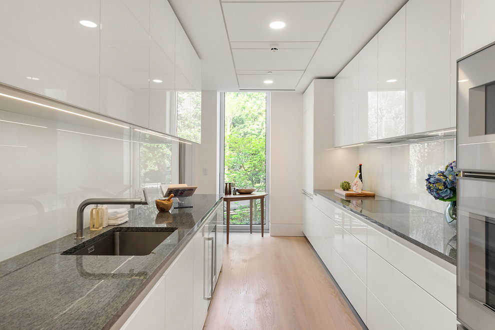 Design ideas for a contemporary galley kitchen in London with a submerged sink, flat-panel cabinets, white cabinets, white splashback, glass sheet splashback, stainless steel appliances, light hardwood flooring and no island.