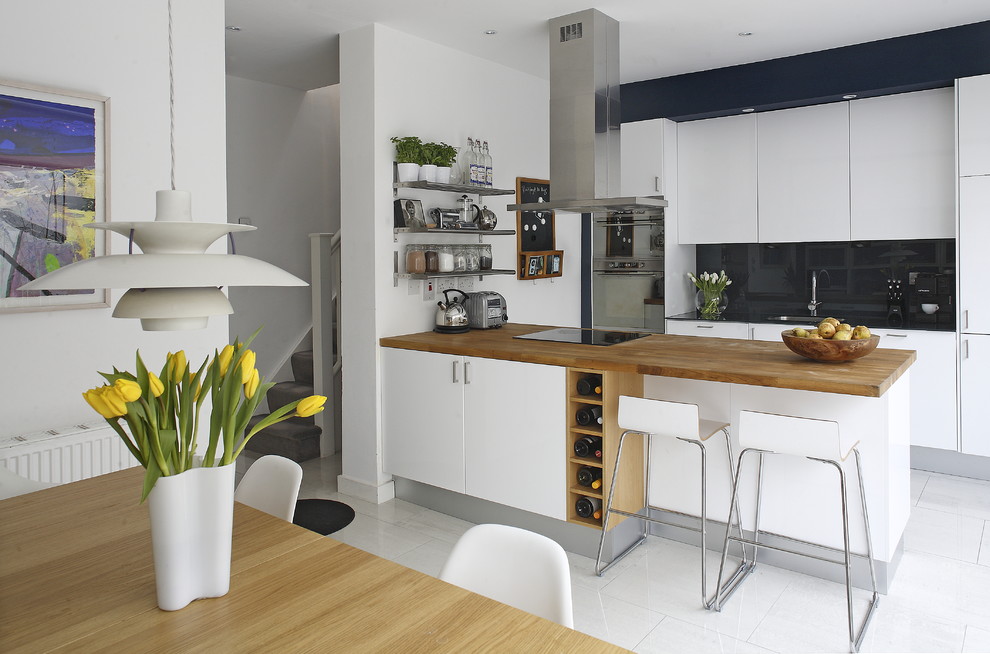 Trendy galley eat-in kitchen photo in Dublin with stainless steel appliances, wood countertops, flat-panel cabinets, white cabinets, black backsplash, glass sheet backsplash and brown countertops