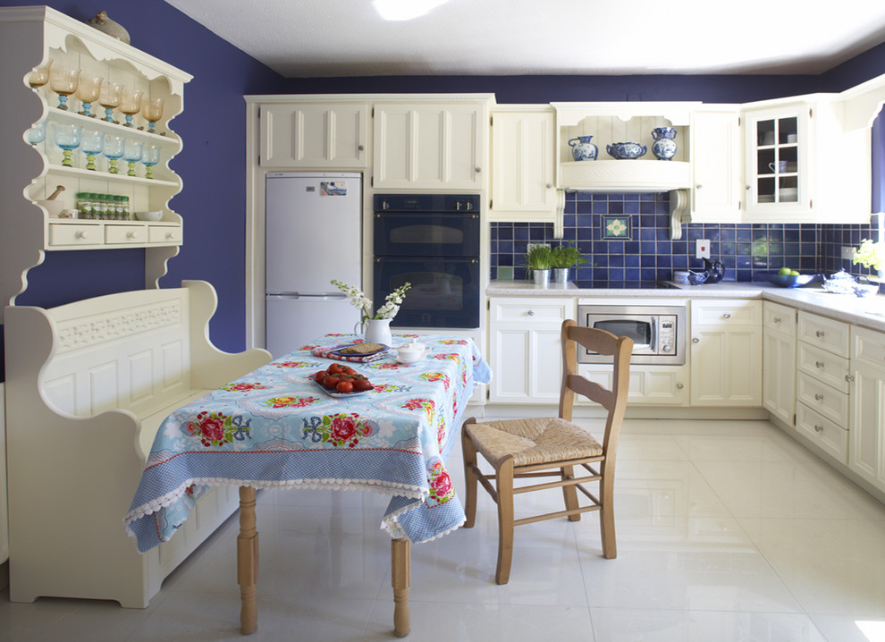 Источник вдохновения для домашнего уюта: угловая кухня в стиле кантри с обеденным столом, фасадами с утопленной филенкой, белыми фасадами и синим фартуком