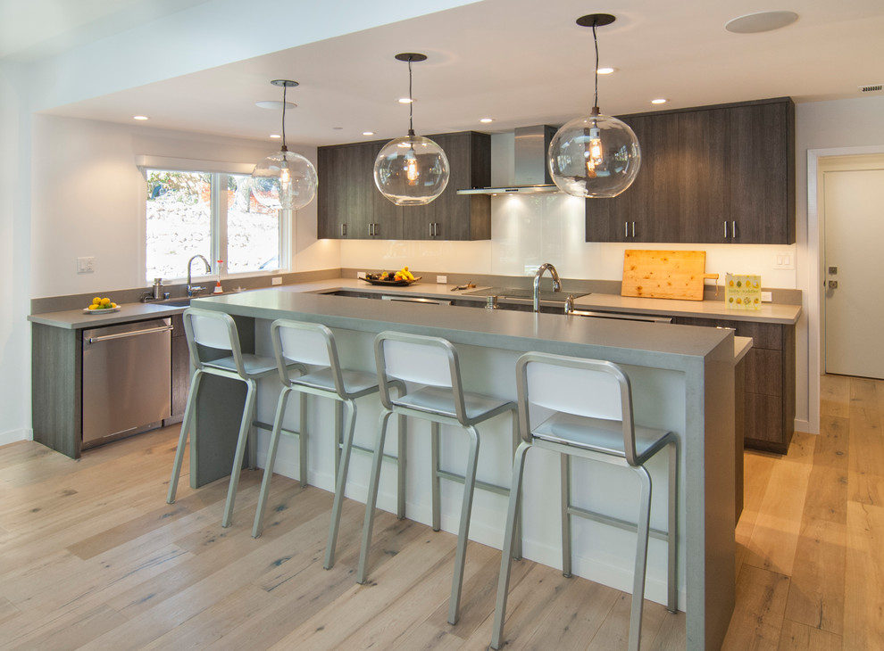 Cette photo montre une cuisine tendance en bois brun avec un placard à porte plane, une crédence blanche, un électroménager en acier inoxydable, parquet clair, îlot et un sol beige.