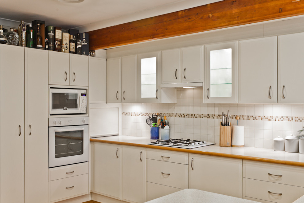 Modern inredning av ett kök, med luckor med upphöjd panel, vita skåp, laminatbänkskiva, vitt stänkskydd, stänkskydd i mosaik och vita vitvaror