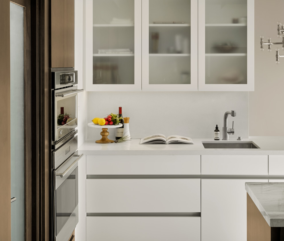 Inspiration för små moderna kök, med en undermonterad diskho, luckor med glaspanel, vita skåp, vitt stänkskydd, rostfria vitvaror och en köksö