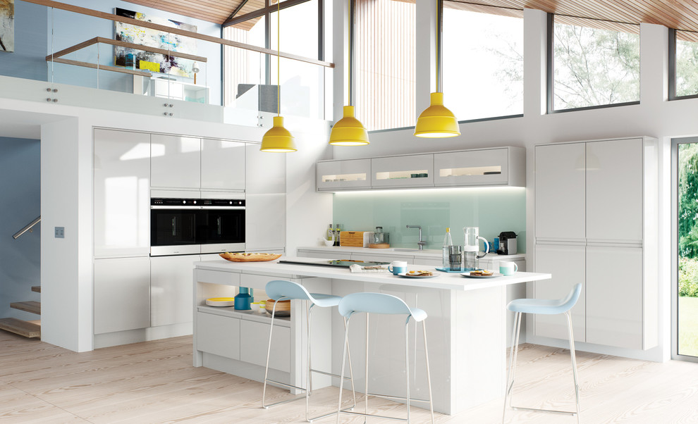 Photo of a large contemporary u-shaped open plan kitchen in Sussex with a submerged sink, flat-panel cabinets, white cabinets, blue splashback, glass tiled splashback, white appliances, light hardwood flooring, a breakfast bar and beige floors.