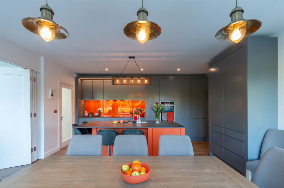 Moderne Wohnküche mit flächenbündigen Schrankfronten, grauen Schränken, Küchenrückwand in Orange, Glasrückwand und Kücheninsel in Sonstige