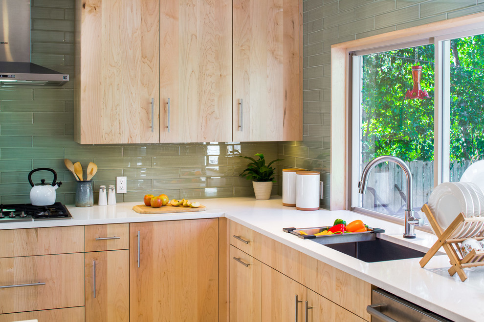 Esempio di una cucina minimal con lavello sottopiano, ante lisce, ante in legno chiaro, top in superficie solida, paraspruzzi verde, paraspruzzi con piastrelle di vetro, elettrodomestici in acciaio inossidabile e pavimento in gres porcellanato
