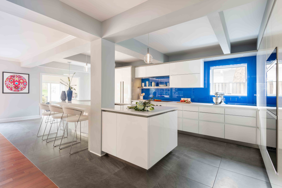 Свежая идея для дизайна: угловая кухня в современном стиле с врезной мойкой, плоскими фасадами, белыми фасадами, синим фартуком, фартуком из стекла, островом, серым полом, белой столешницей и балками на потолке - отличное фото интерьера